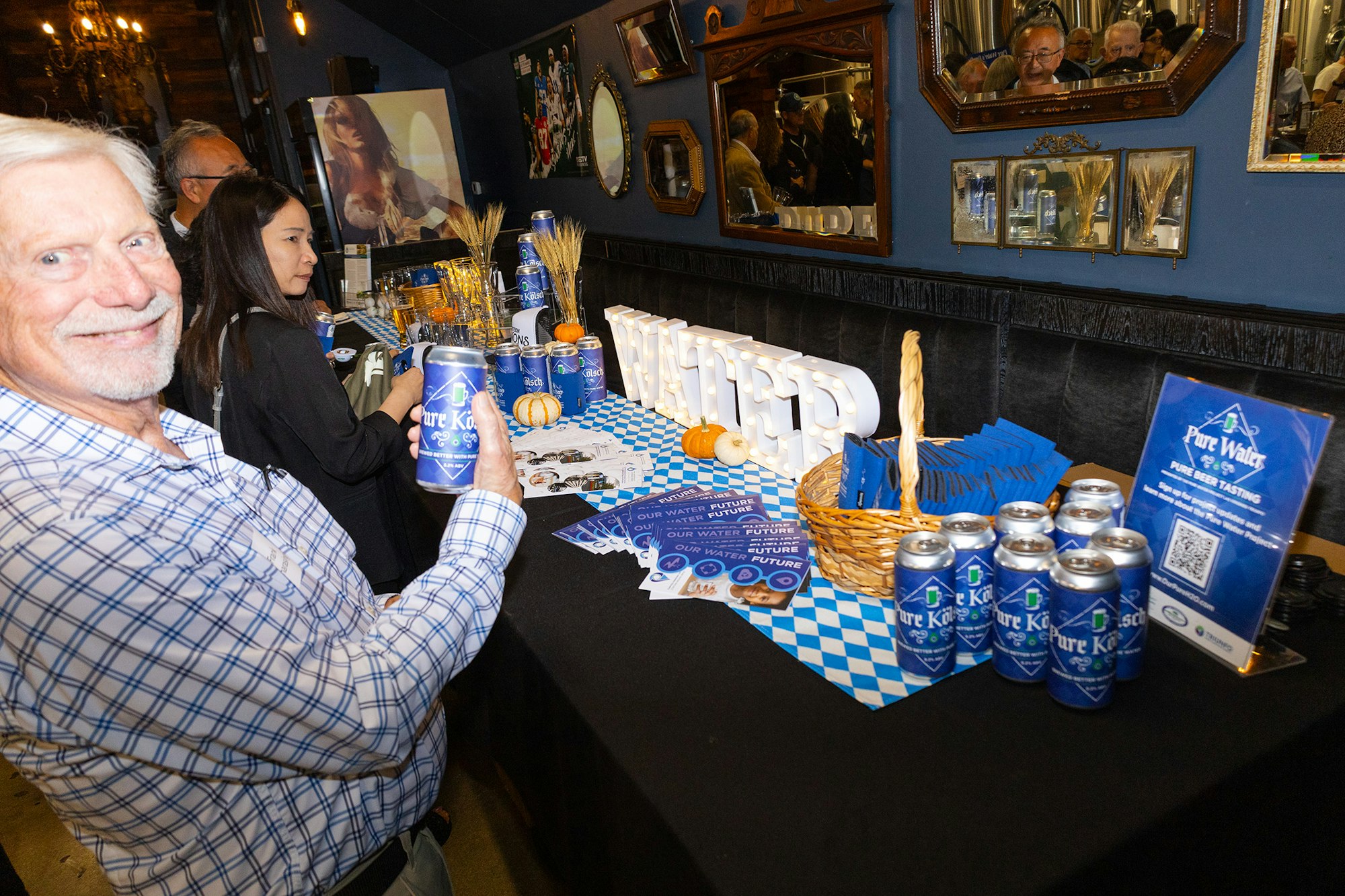 An event scene with a man holding a beer can, a promotional table featuring beverages, decor, and informational materials.