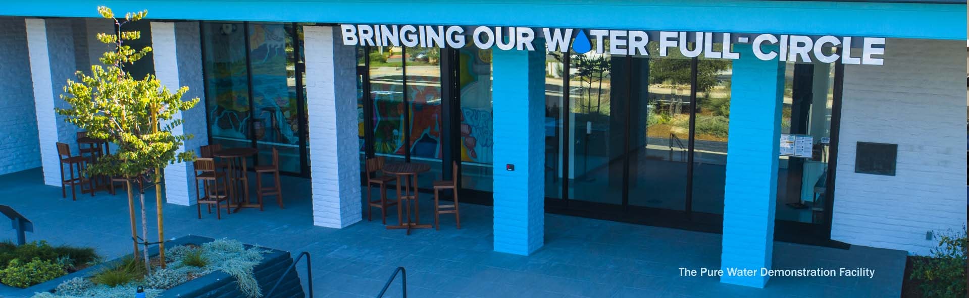 Modern blue and white building facade with the text "BRINGING OUR WATER FULL CIRCLE" above entrance.