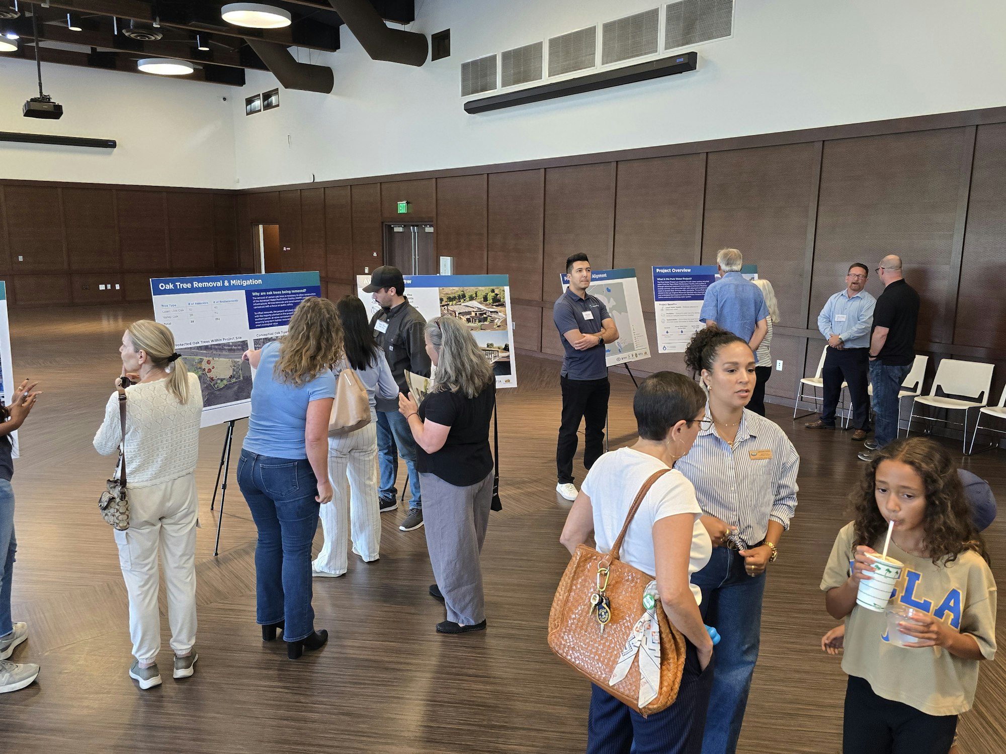 People are gathered in a hall discussing posters about oak tree removal and project management.
