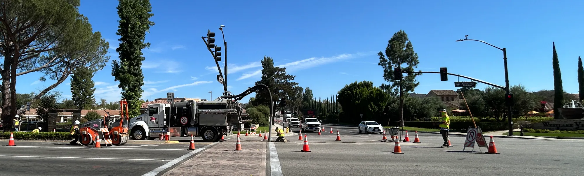 Road construction scene with traffic cones, construction equipment, and signs indicating a closed sidewalk and to use the crosswalk.