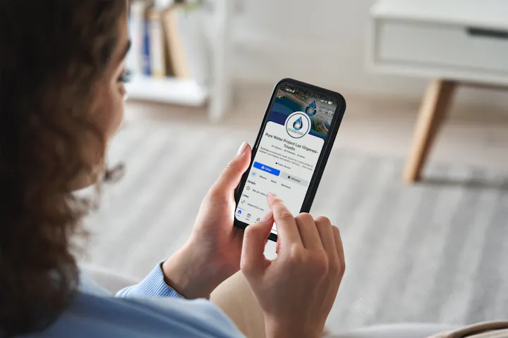 A person using a smartphone to view the "Pure Water Project" Facebook page, focused on water sustainability.
