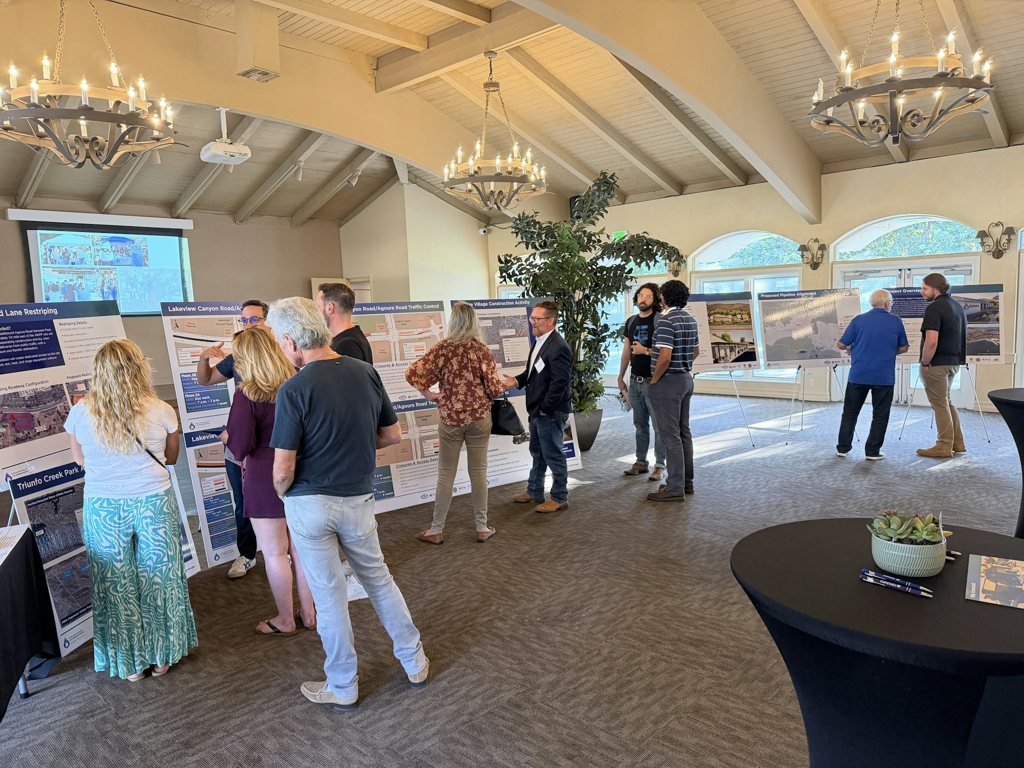 People are engaging in a community event, discussing project displays on posters inside a well-lit venue.
