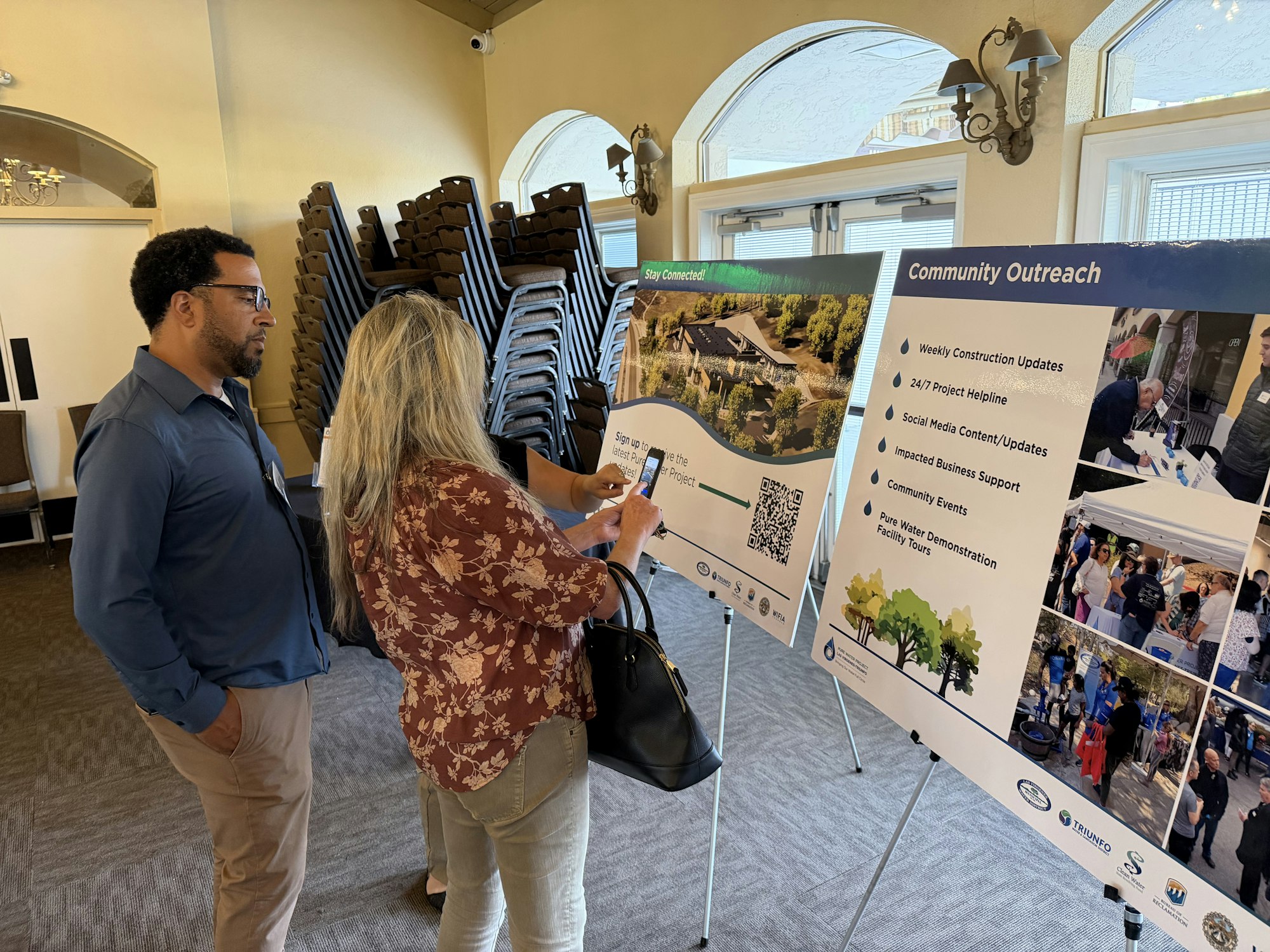 Two people engage with community outreach posters detailing construction updates, project helplines, and events.