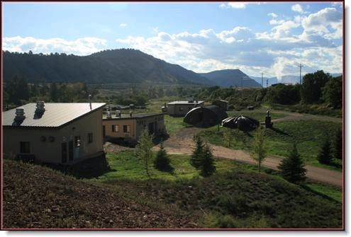Rural landscape with buildings, hills, and a cloudy sky.