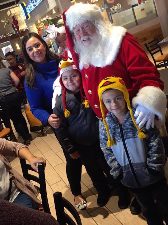 A person dressed as Santa Claus with two kids and a woman, indoors, likely celebrating the holiday season.
