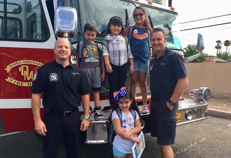 A group of children with two firefighters in front of a fire truck.