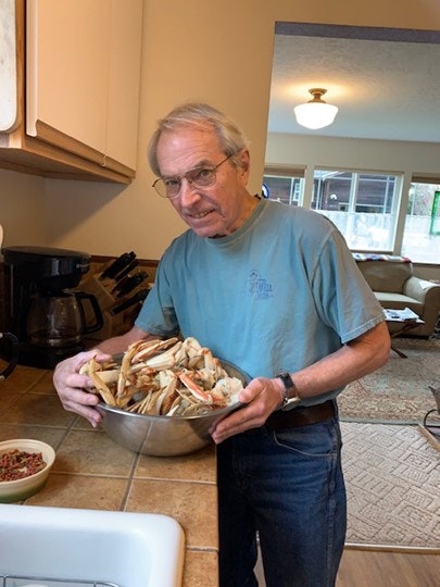 A man holding a bowl of crab legs, inside a kitchen.