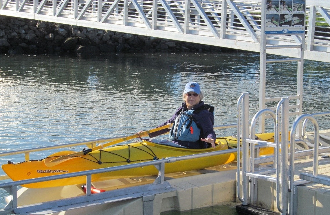 Person in a yellow kayak by a dock with a bridge overhead.