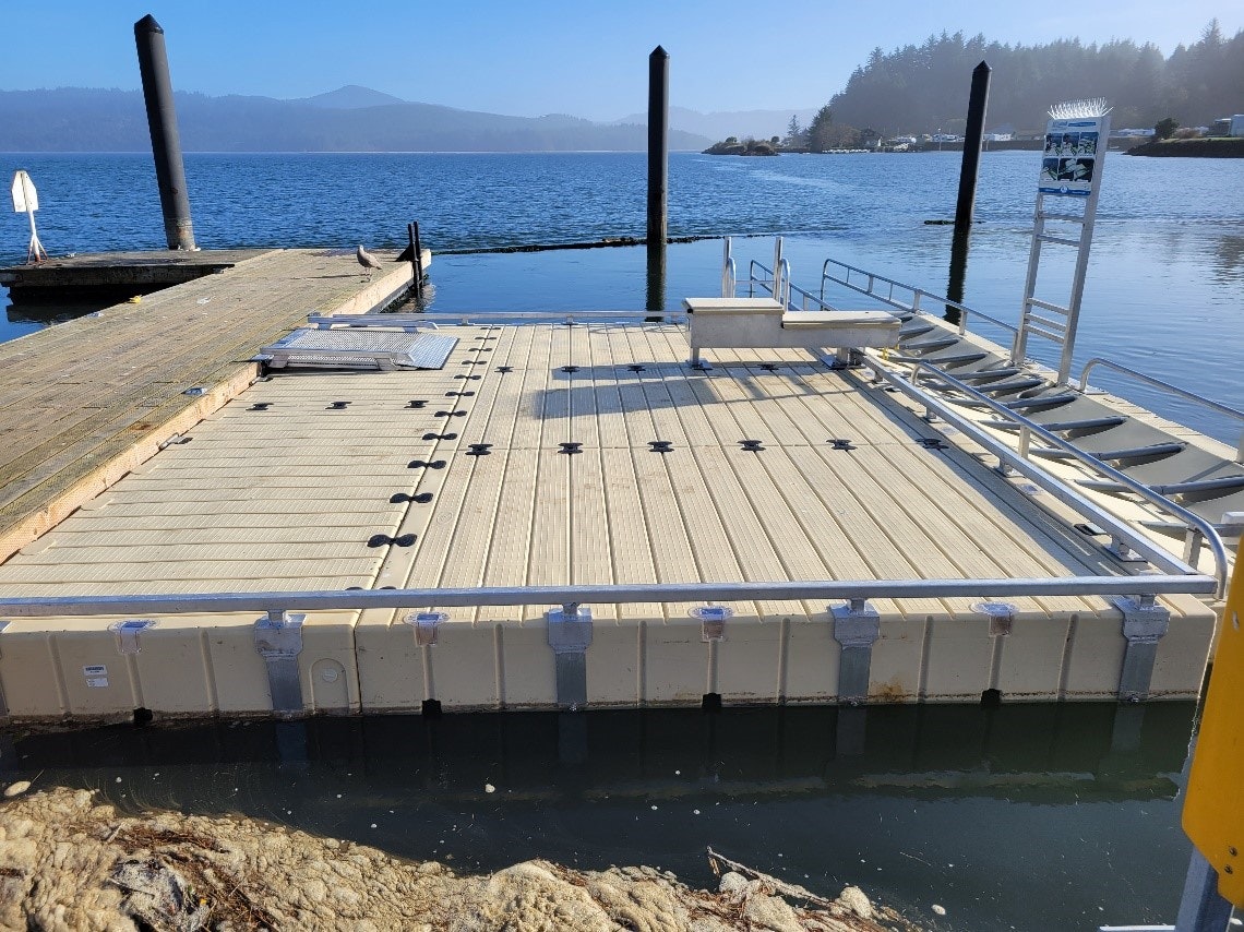 Floating dock on a calm lake with mountains in the background on a sunny day.