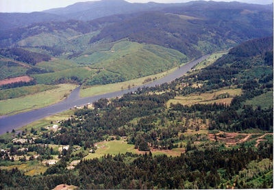 A winding river cuts through a lush, green valley with scattered buildings and trees.