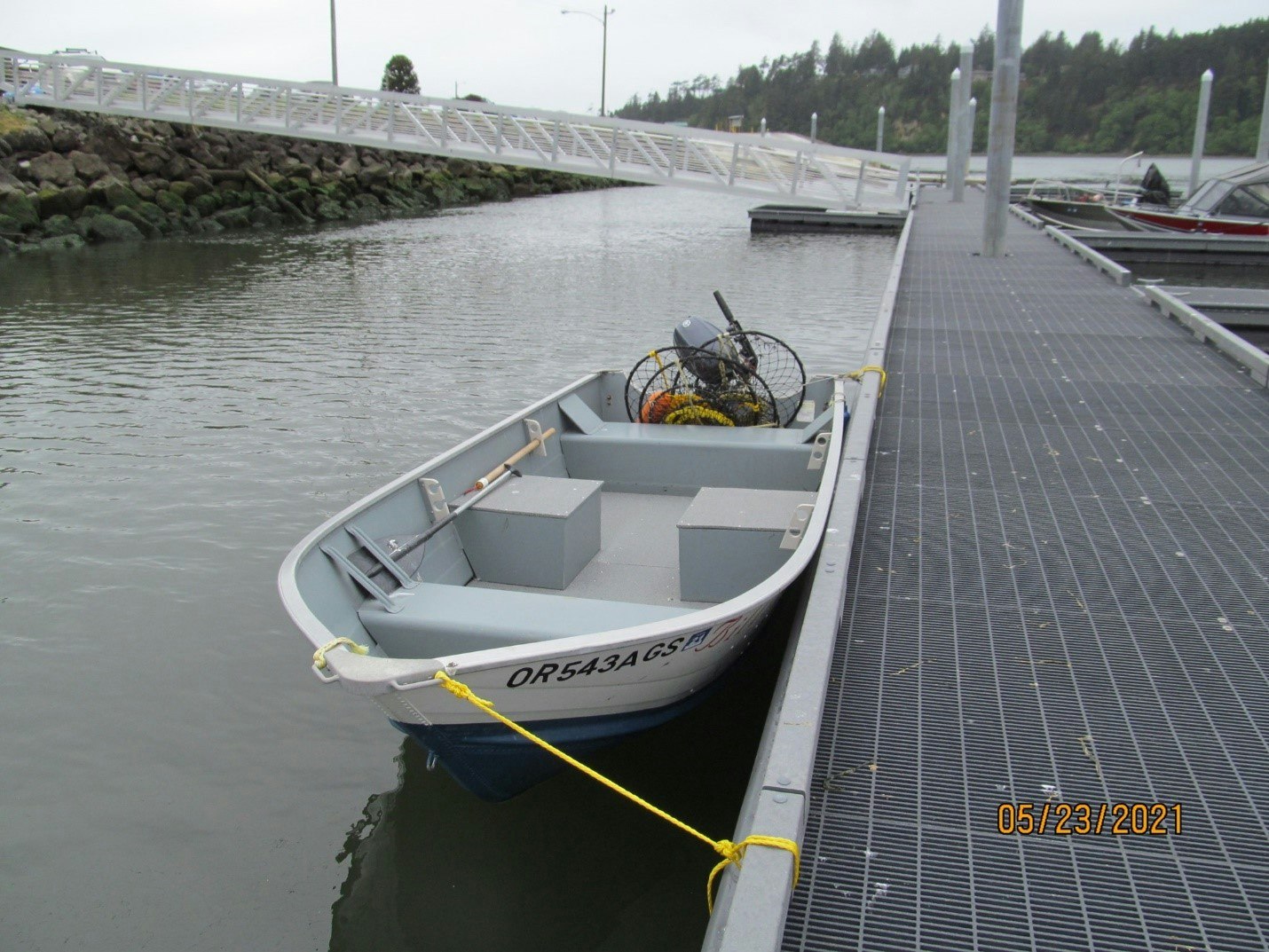 A boat tied to a dock with crabbing gear inside, near a pedestrian bridge over water.