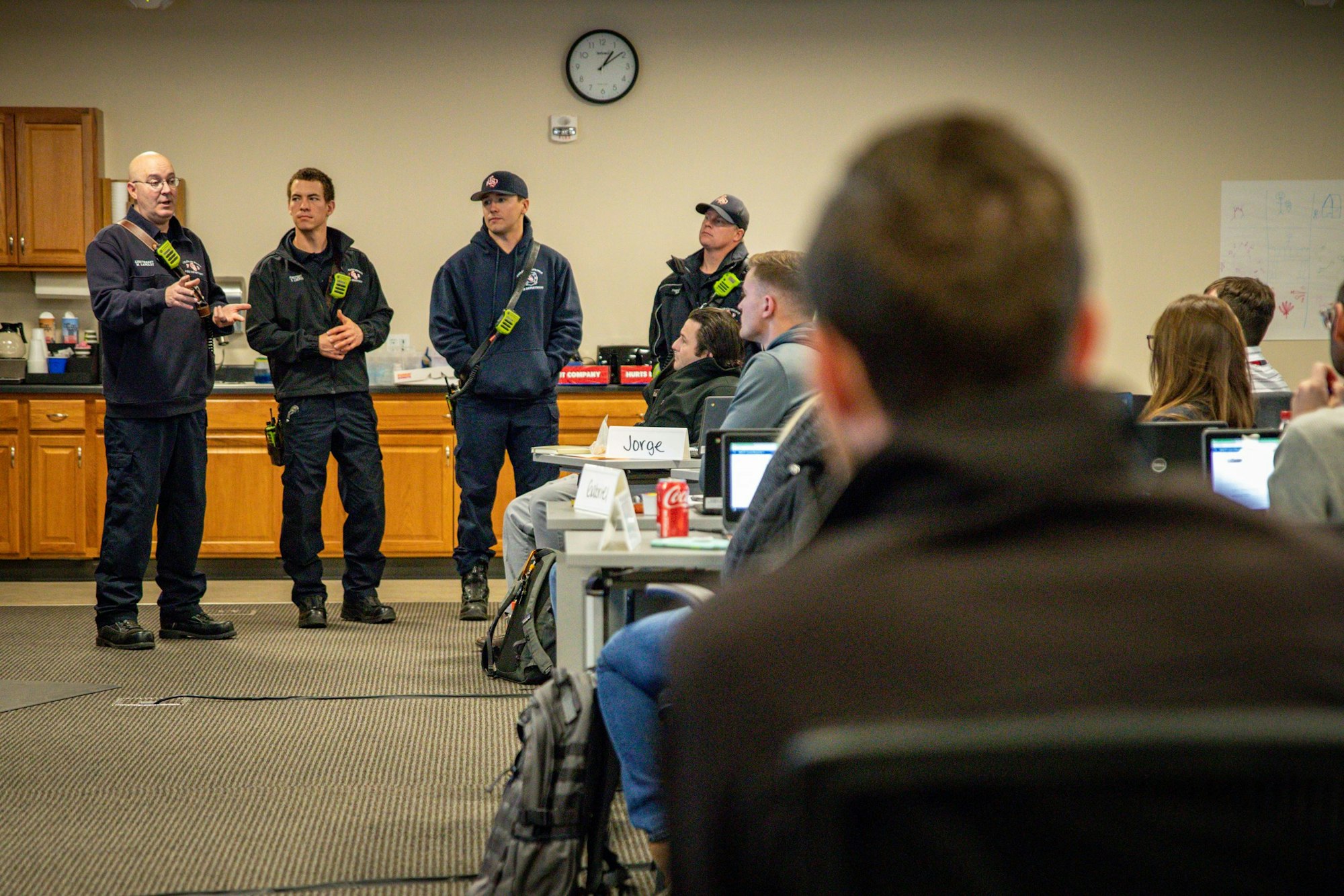 A group of people in uniform speak to an audience in a classroom setting.