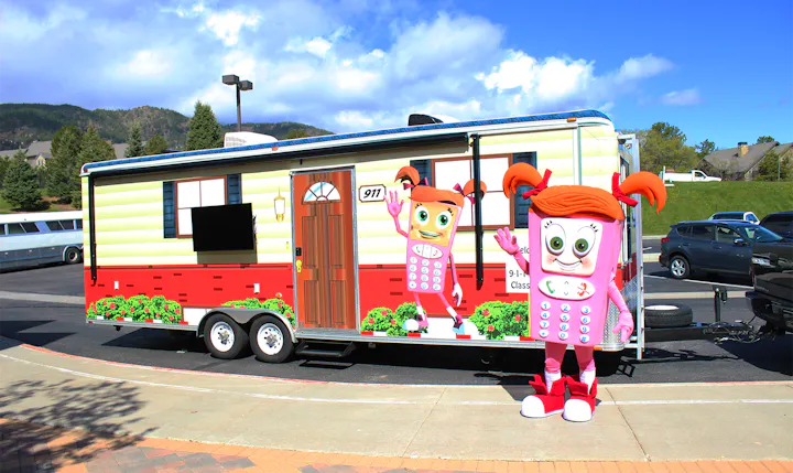 Cartoon-themed trailer and a person in a similar mascot costume outdoors, with mountains and trees in the background.
