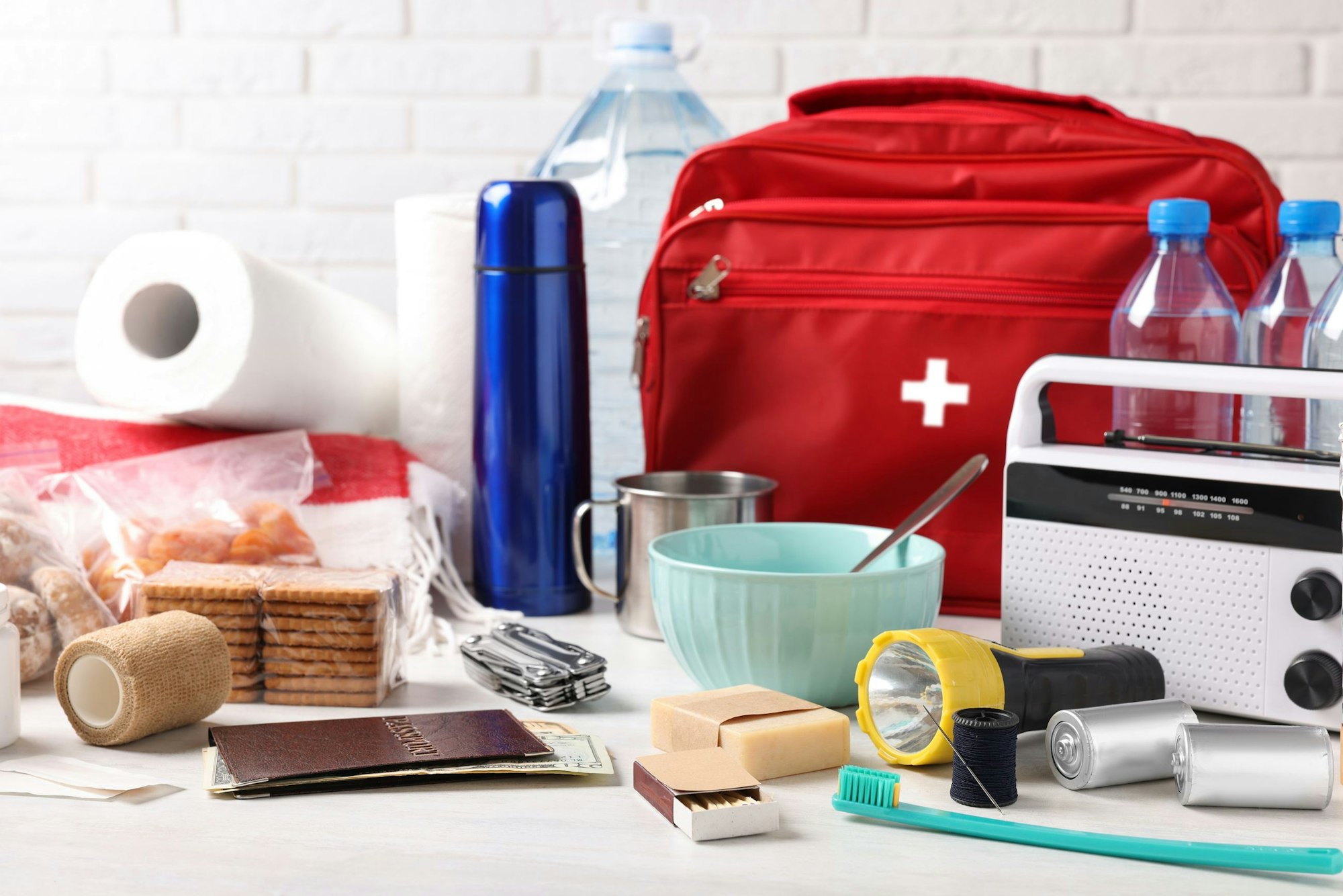 Emergency kit items: red bag, flashlight, radio, bottled water, thermos, toiletries, crackers, first aid supplies, and a metal cup.