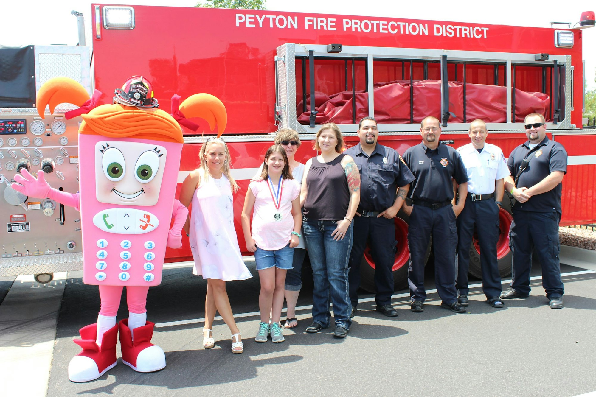 A group of people, including a costumed character, standing in front of a Peyton Fire Protection District fire truck.