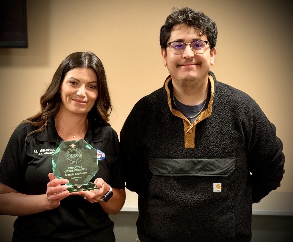 Two people standing, one holding an "Employee of the Quarter" award.