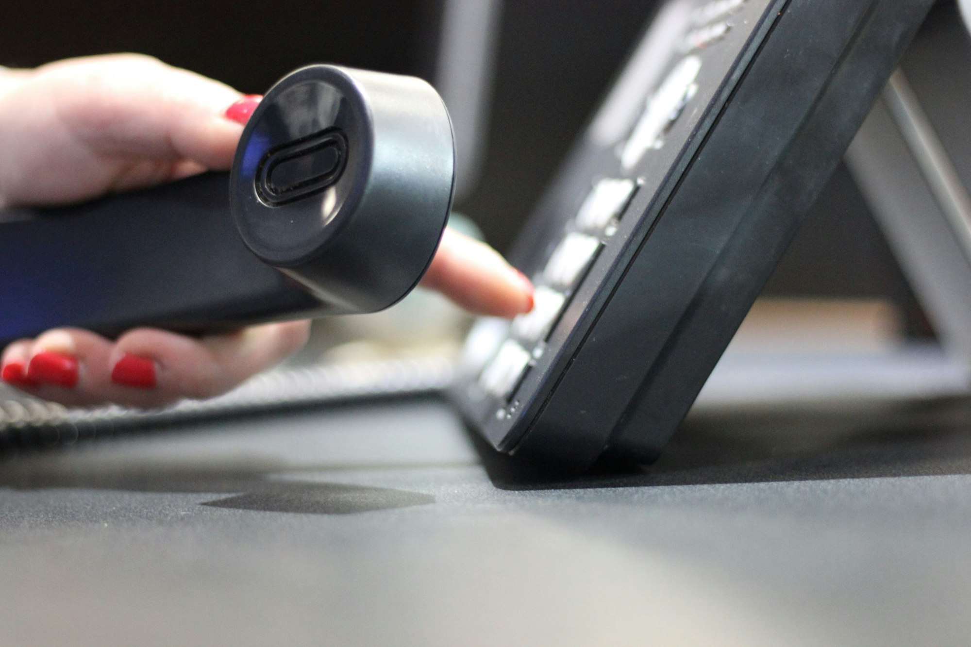 A hand using a landline phone, pressing a button with the other hand.