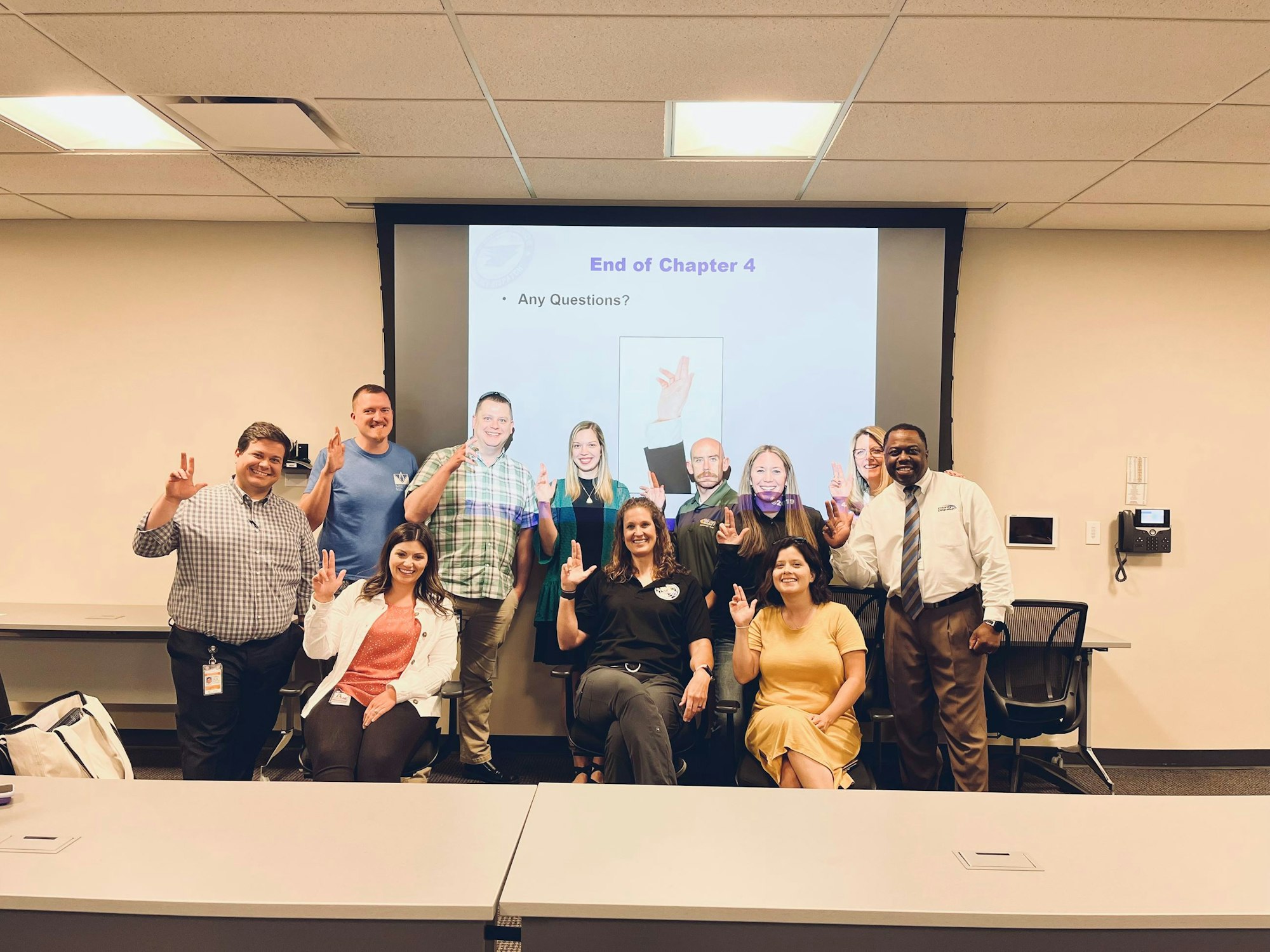 A group of people posing in front of a presentation screen displaying "End of Chapter 4 - Any Questions?"