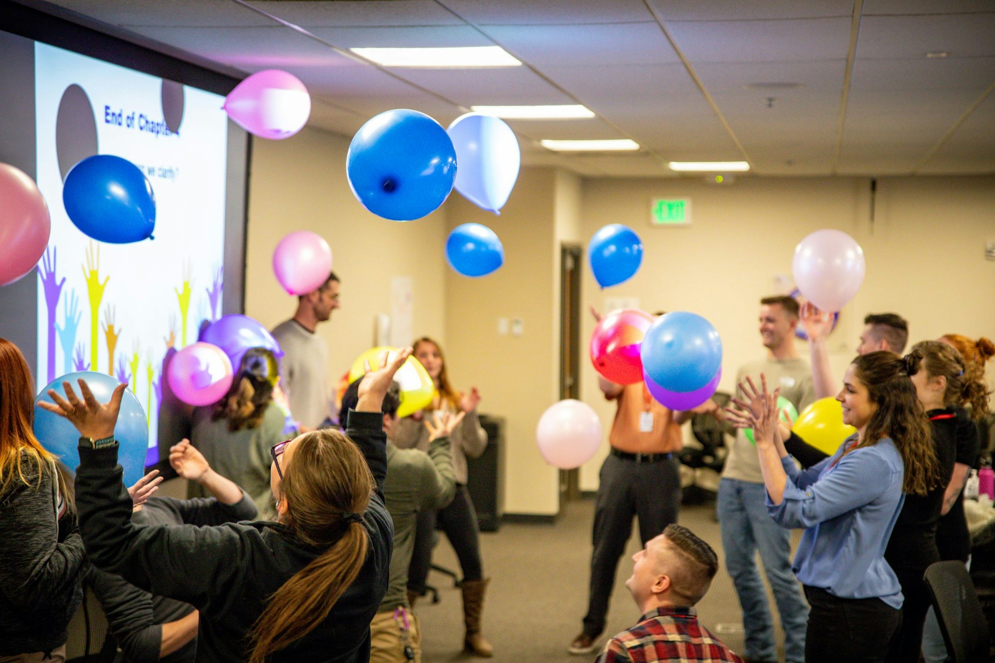 People in a room tossing colorful balloons during a presentation.