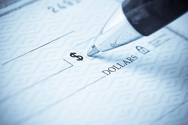 A close-up of a check with a pen poised above the dollar amount field, indicating a transaction or payment.
