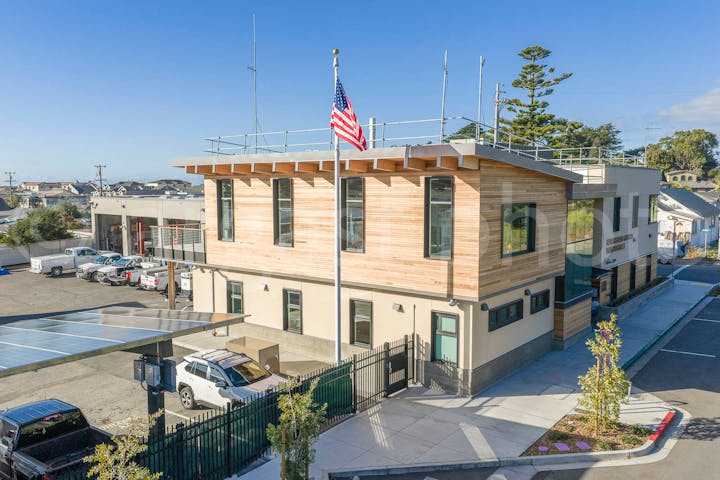 A modern building with a wooden facade, an American flag, and solar panels, situated in a parking area under a clear sky.
