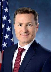 A man in a suit and tie is standing in front of an American flag.