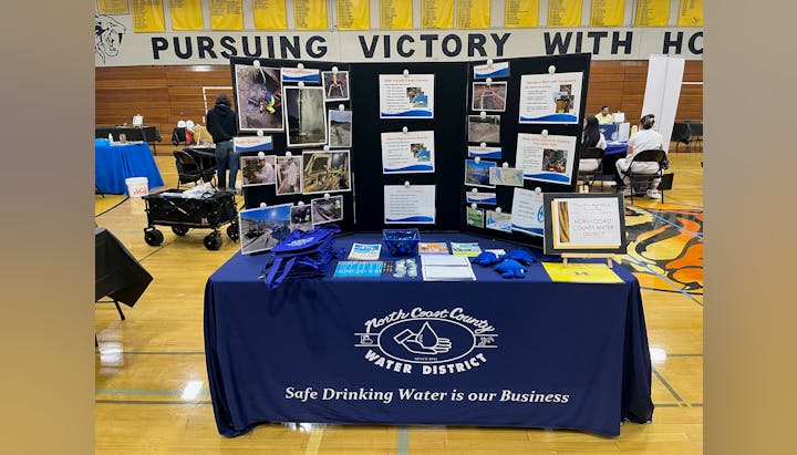 A booth for the North Coast County Water District showcasing water quality and engineering, featuring photos, brochures, and giveaways.