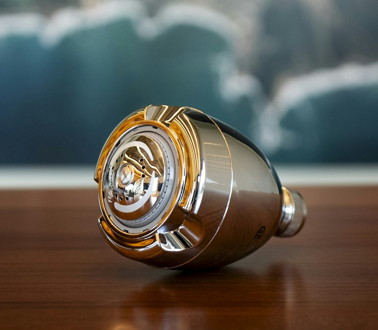 The image shows a shiny, metallic object resembling a part of a mechanical device or tool, resting on a wooden surface.