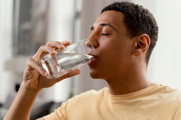A person is drinking water from a glass, enjoying a moment of hydration indoors.