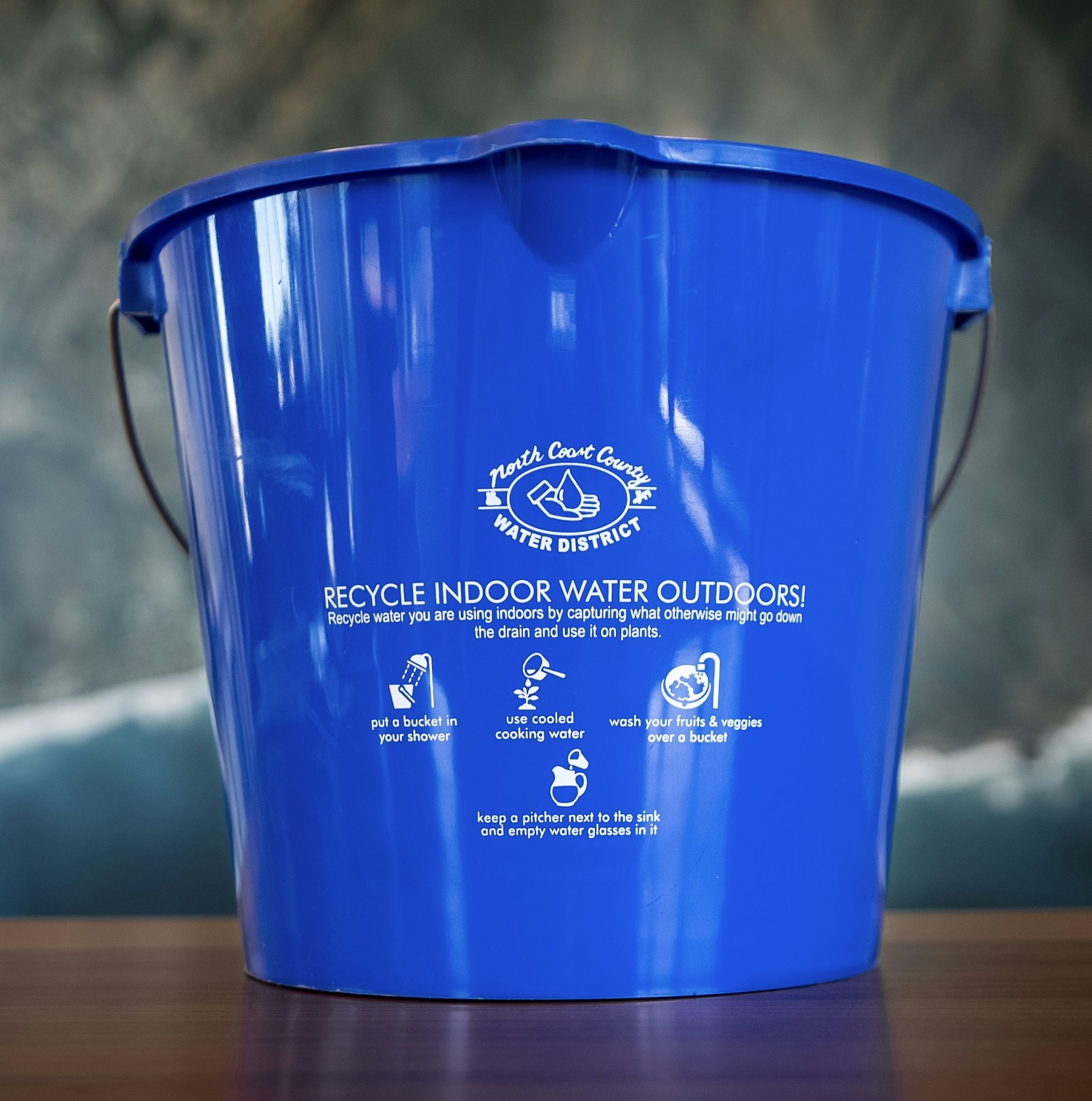 A blue bucket promoting water recycling tips from the North Coast County Water District for indoor use.