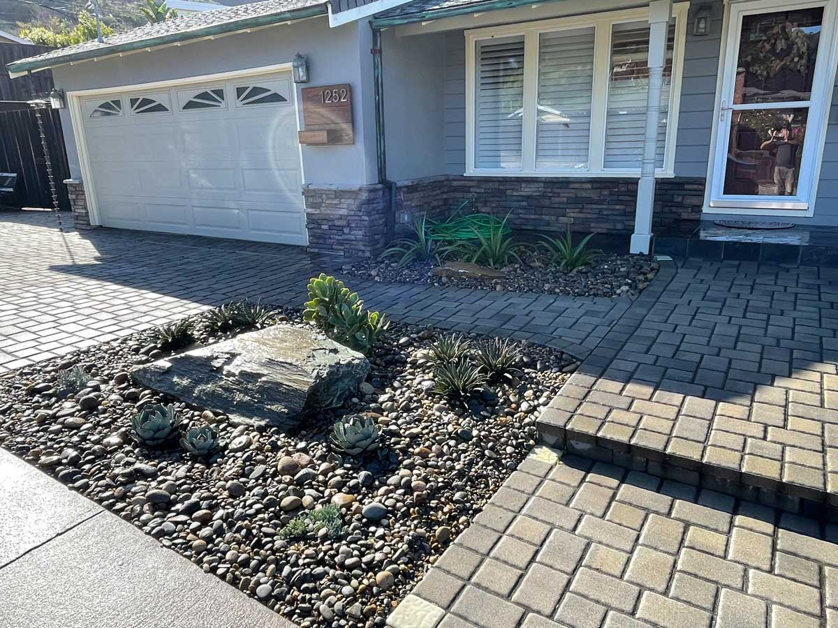 House facade with garage, stone walkway, and garden area featuring rocks and succulents.
