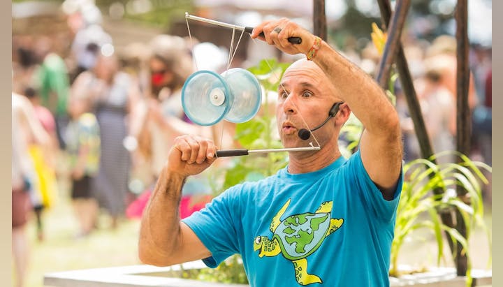 A performer in a blue shirt is entertaining an audience with a diablo, showcasing skill and excitement in a lively outdoor setting.