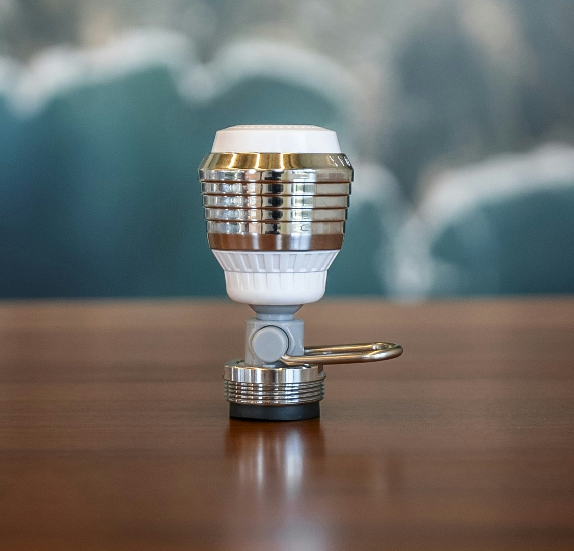 The image shows a stylish light bulb with a metallic design, mounted on a gray base, resting on a wooden table.
