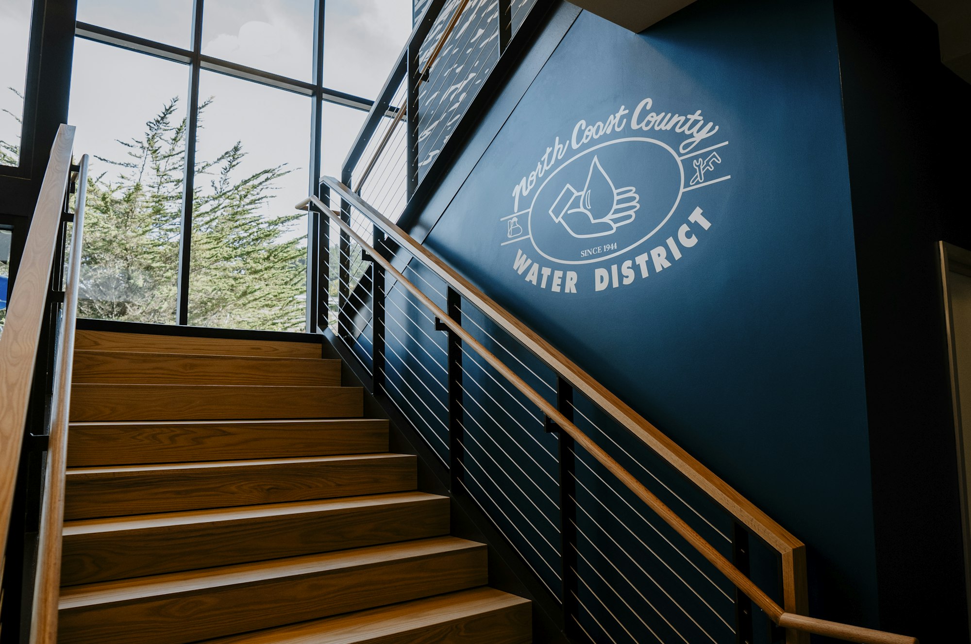 The image features a modern stairway leading up to a wall displaying the "North Coast County Water District" logo and branding.