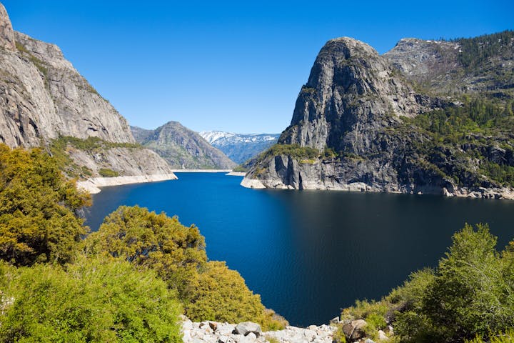 A scenic view of a lake surrounded by mountains and lush greenery under a clear blue sky.