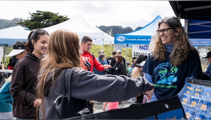 A lively outdoor event with people interacting at booths, likely focused on environmental awareness or community engagement.