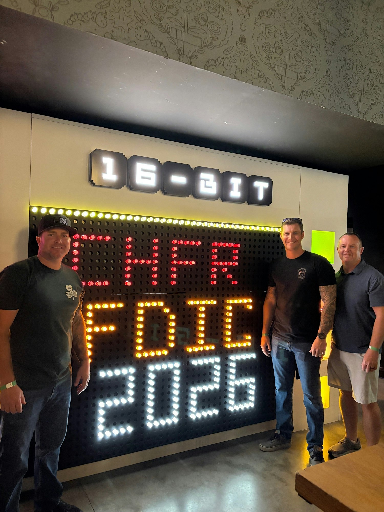 Three men pose in front of a colorful display that reads "16-BIT CHFR FDIC 2026."