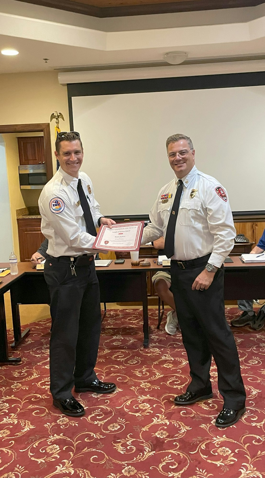 Two individuals in formal attire exchanging a certificate.