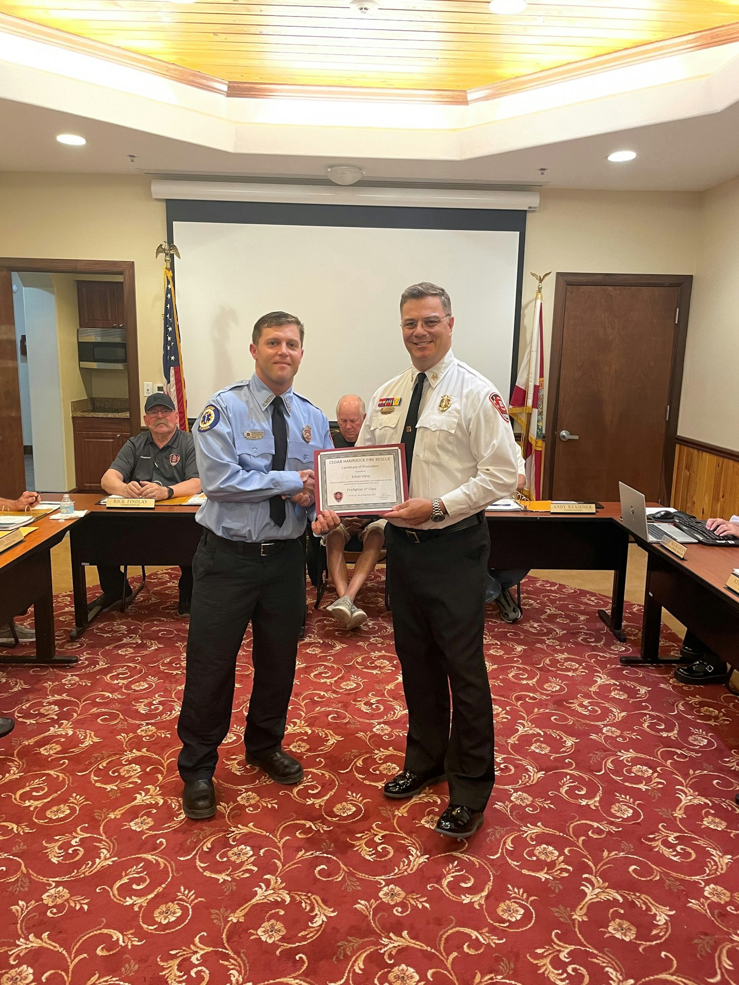 Two men posing with a certificate, likely at a formal award or recognition ceremony.