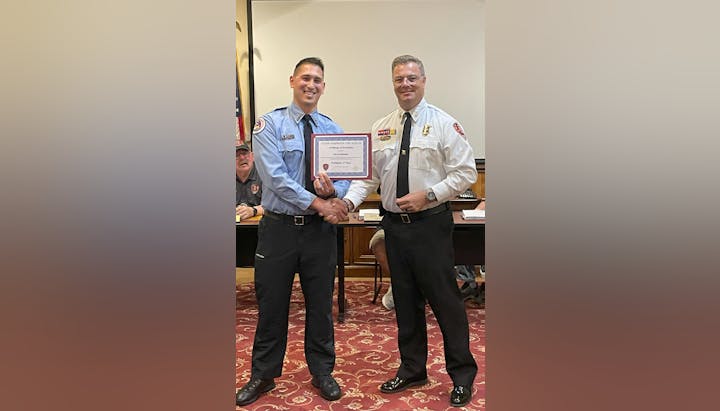 Two men in uniform shaking hands, one holding a certificate of promotion.