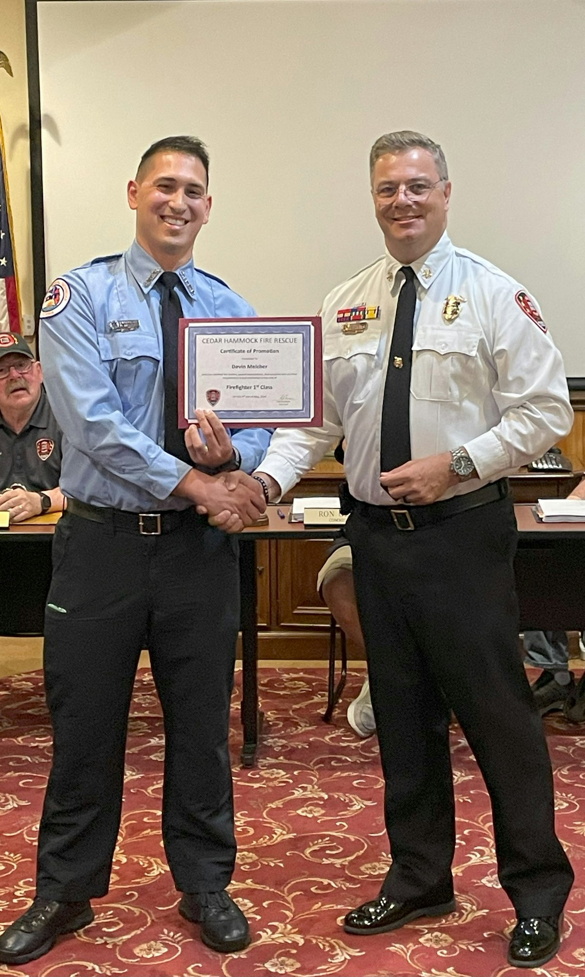 Two men in uniform shaking hands, one holding a certificate of promotion.