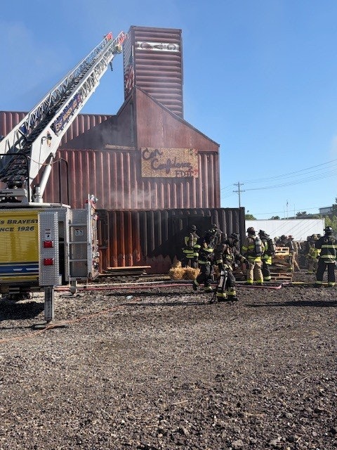 Firefighters are battling a blaze at a large building. Smoke is visible, and a fire truck is on-site assisting with the response.