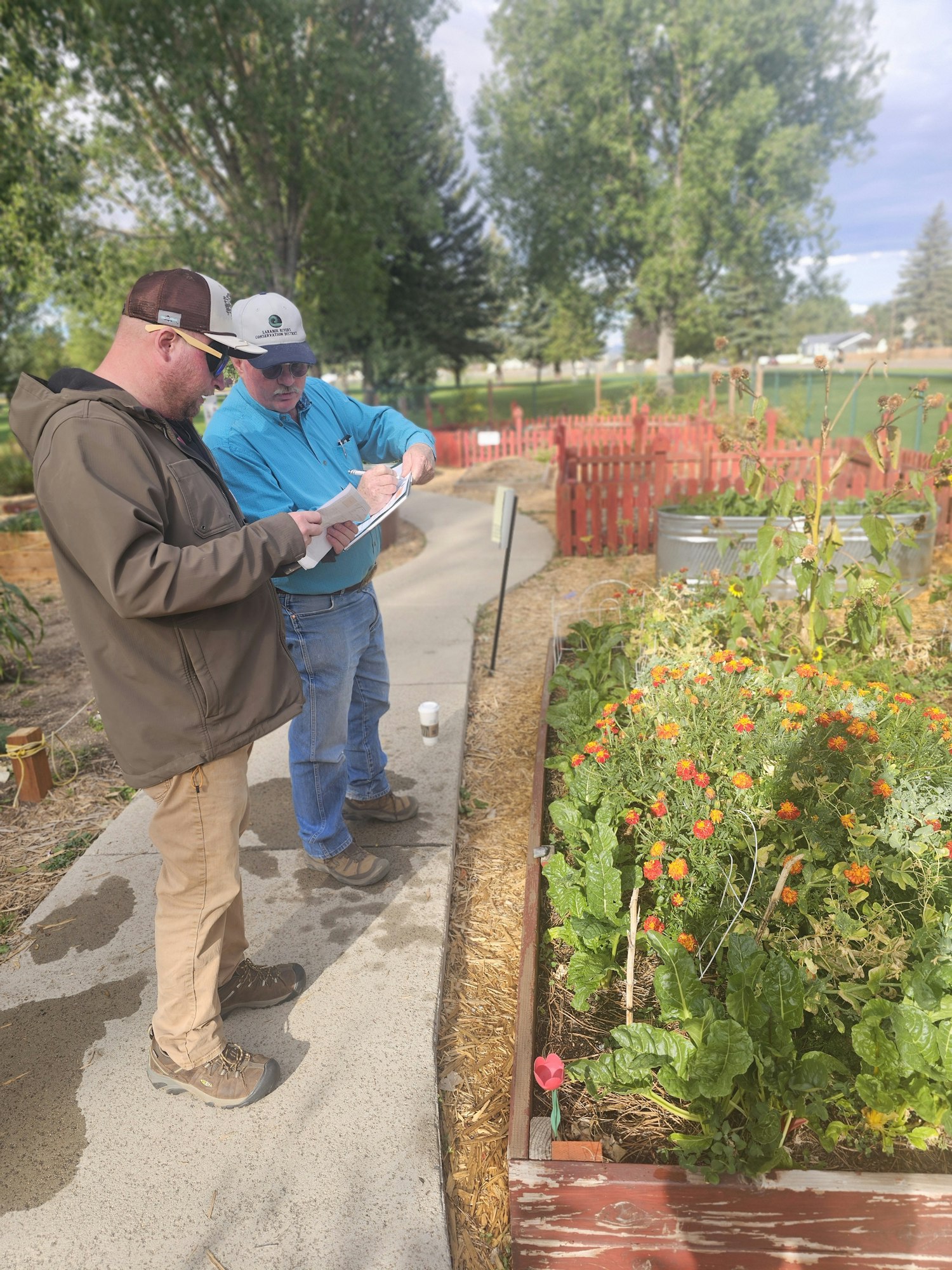 Two people examining a garden with flowers and vegetables along a path.