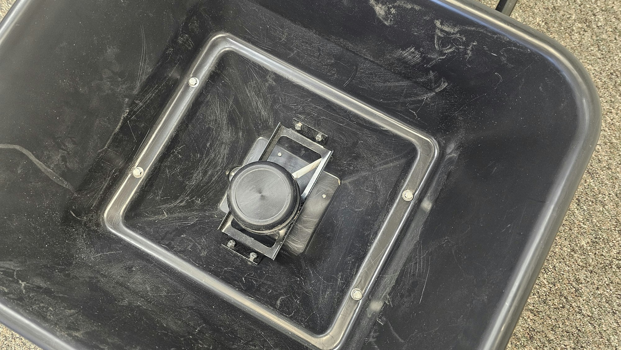 An overhead view of a wheeled bin with a central, square, fixed wheel assembly.