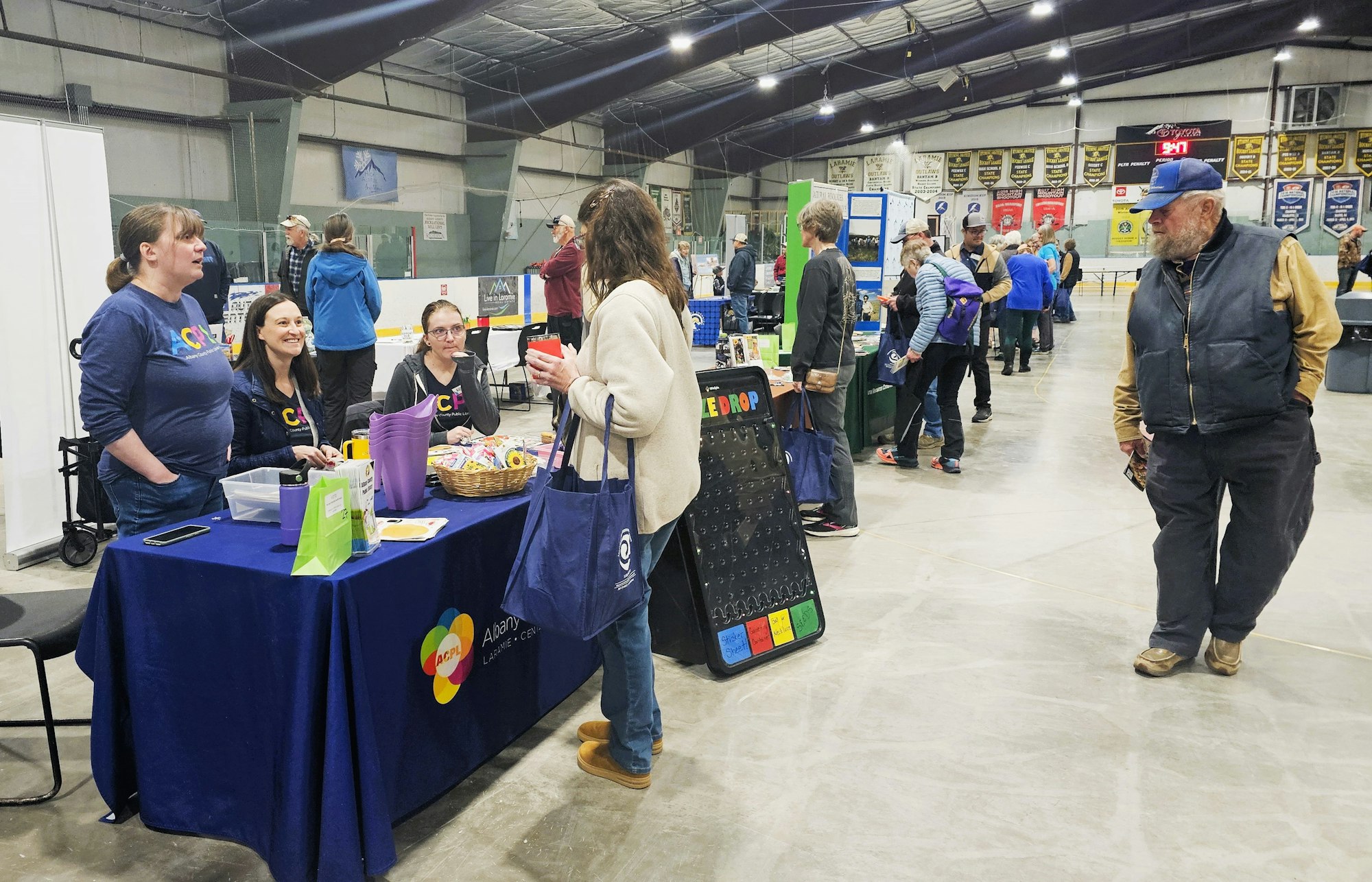 An indoor event with people staffing a booth, attendees walking, and promotional materials on display.