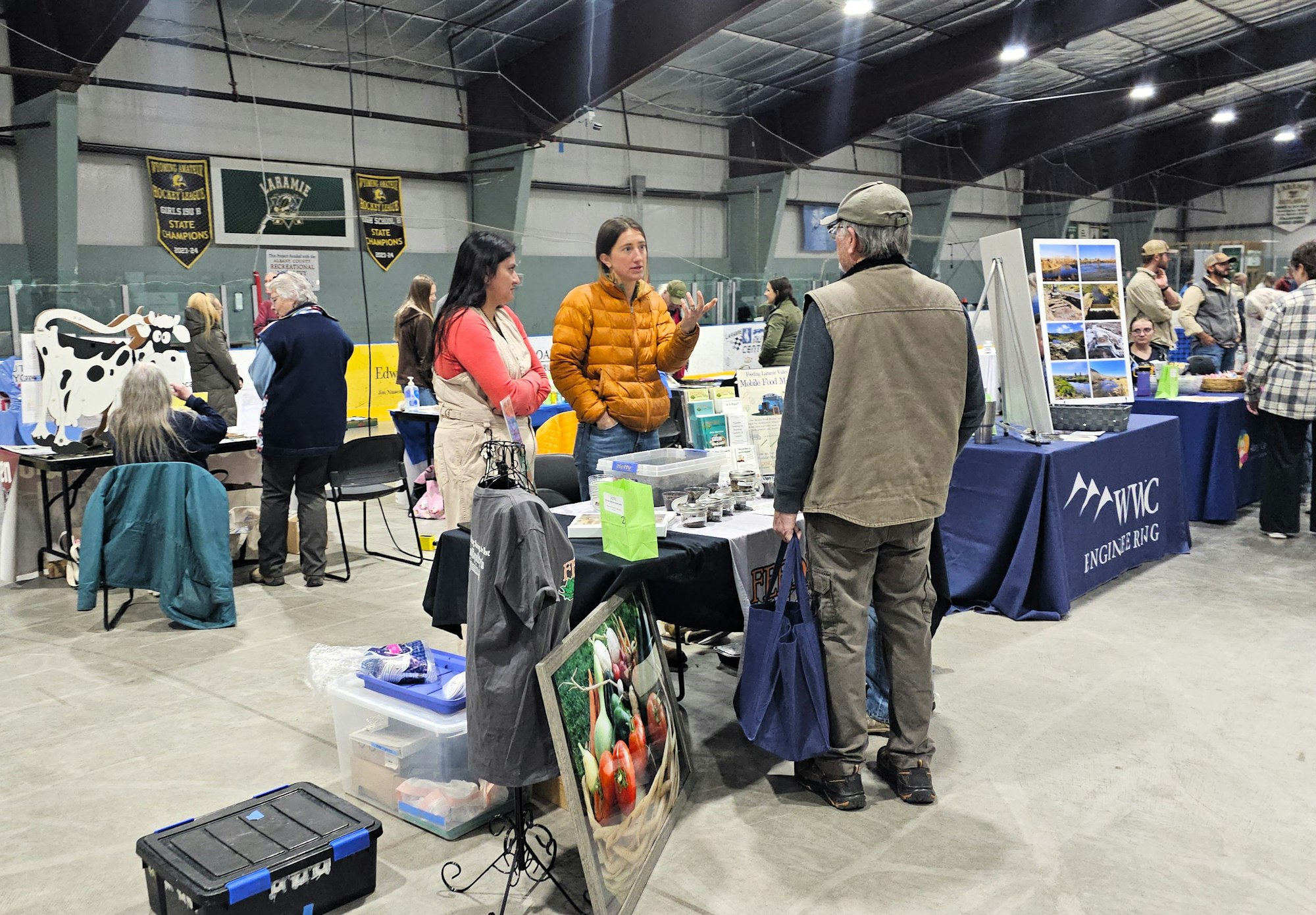Indoor event with booths, people conversing, and agricultural or environmental displays.