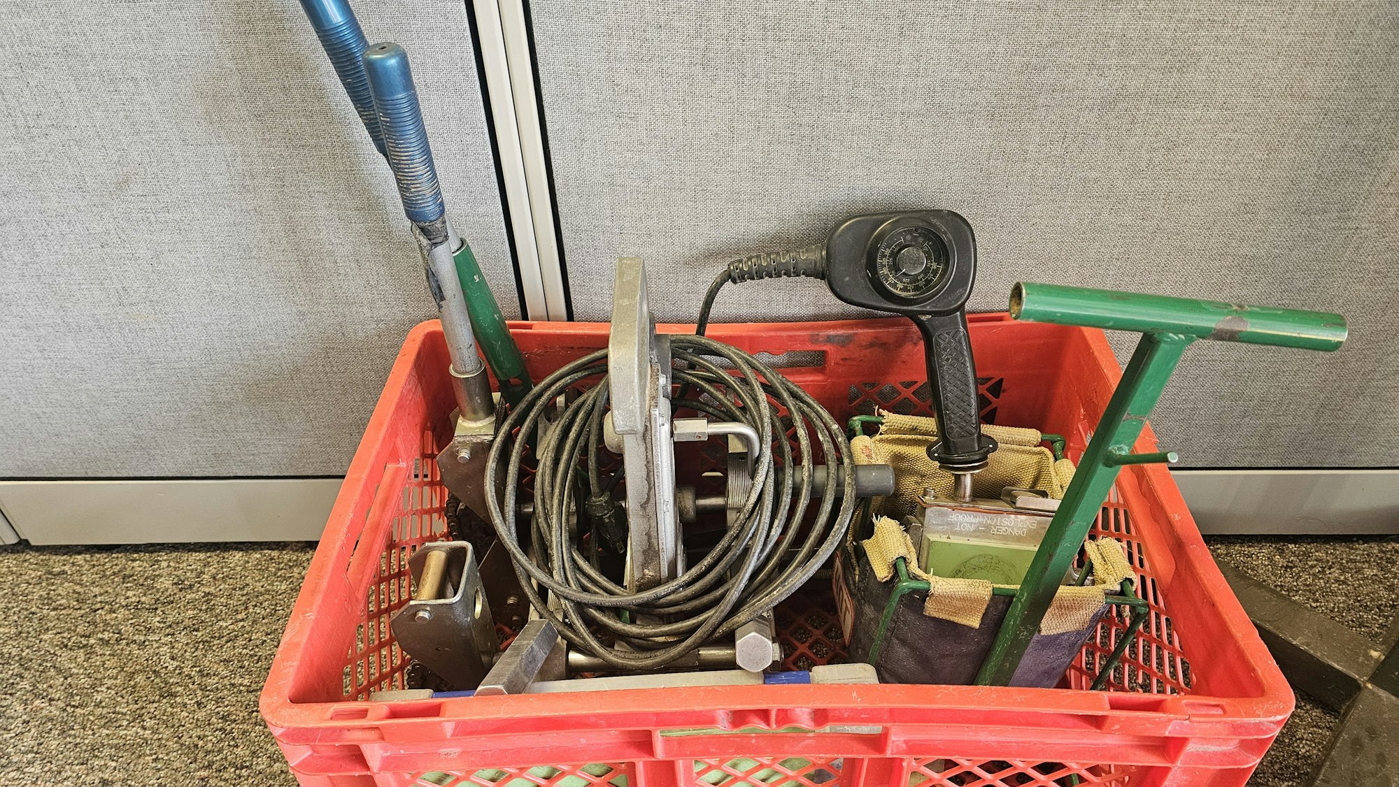 A red crate with various tools and cables, possibly maintenance equipment, on a carpeted floor.