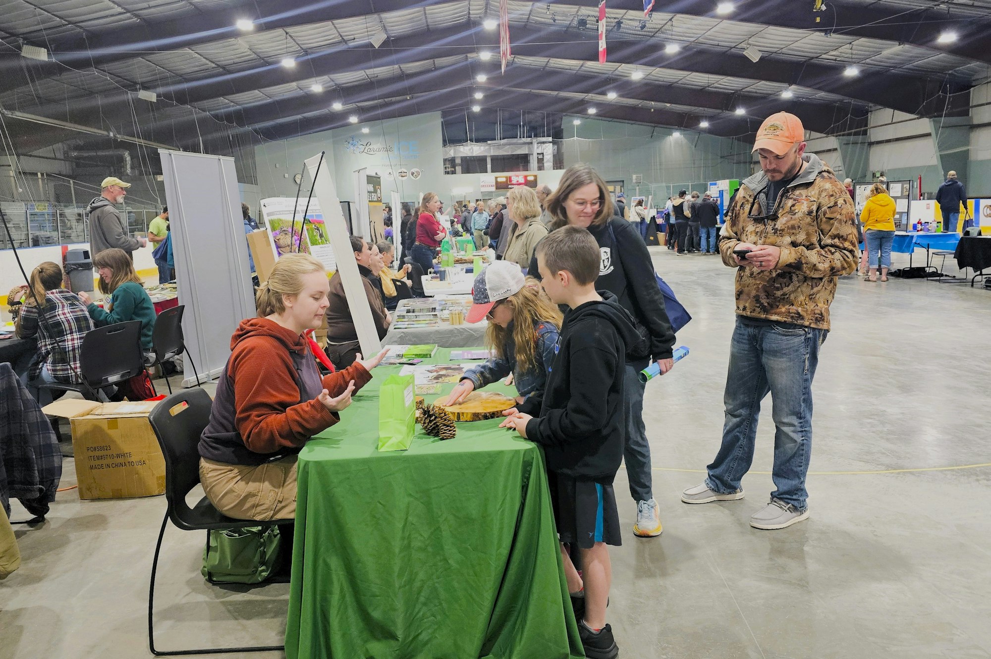 An indoor event with booths, attendees engaging with exhibitors, informational displays, and a casual atmosphere.
