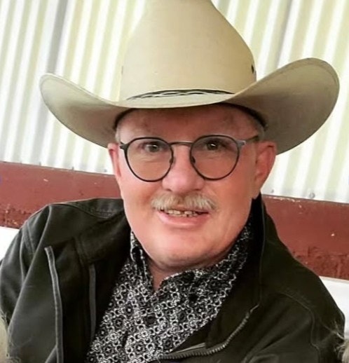 A person wearing a cowboy hat, glasses, and a patterned shirt, smiling at the camera.