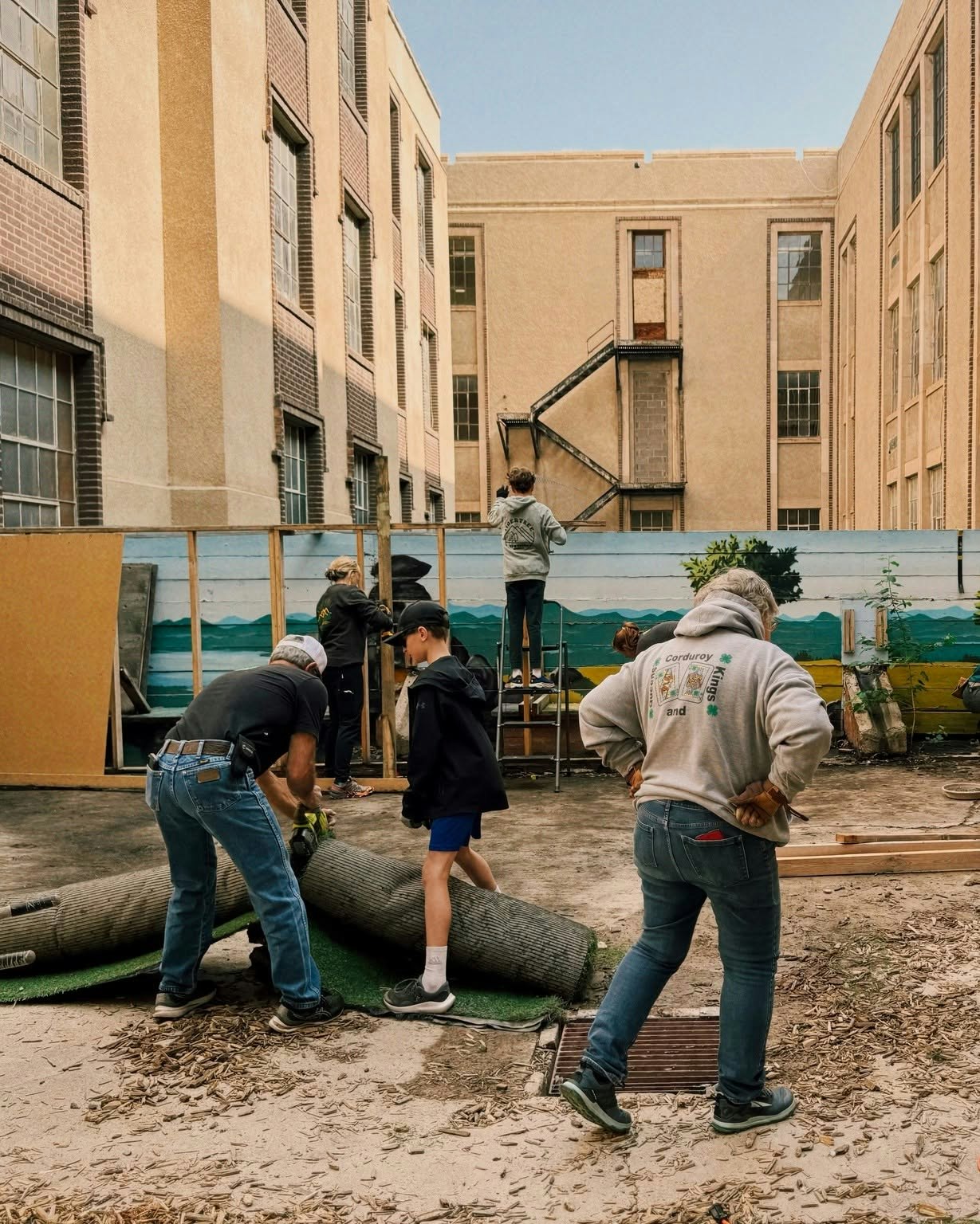 A group of people is working together in a courtyard, setting up structures and handling materials for a project.